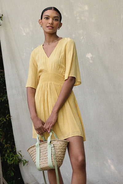 Wear a bit of sunshine with this beautiful yellow smocked mini dress. Featuring a v neckline, smocked waistline, and textured material. Pair with a classic denim jacket for cooler nights. Product Details: 100% Rayon 1/2 Sleeve Smock flared waist Mini length - above the knee Lined from waist down Fit and flare silhouette