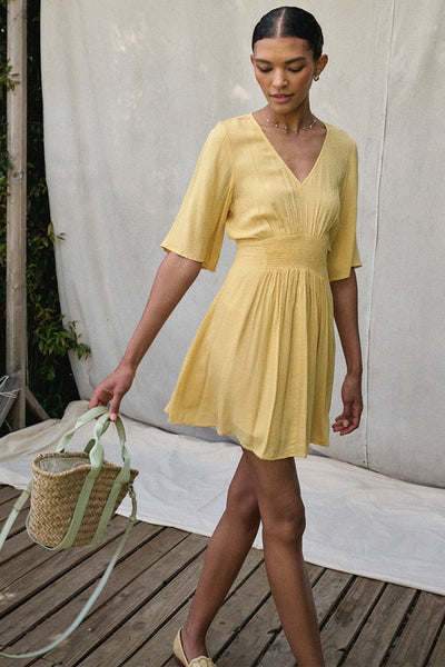 Wear a bit of sunshine with this beautiful yellow smocked mini dress. Featuring a v neckline, smocked waistline, and textured material. Pair with a classic denim jacket for cooler nights. Product Details: 100% Rayon 1/2 Sleeve Smock flared waist Mini length - above the knee Lined from waist down Fit and flare silhouette