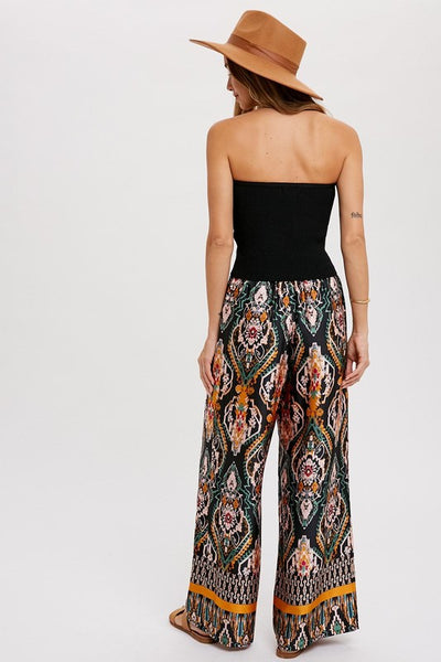 Cool, comfy and versatile! These woven wide leg pants are that and more! Featuring an all over black border print, elastic waist with tassels, and side pockets. Product Details: 100% Polyester Flowy silhouette Side pockets Elastic waist with draw string tie Wide leg