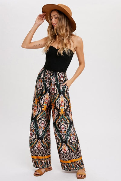 Cool, comfy and versatile! These woven wide leg pants are that and more! Featuring an all over black border print, elastic waist with tassels, and side pockets. Product Details: 100% Polyester Flowy silhouette Side pockets Elastic waist with draw string tie Wide leg