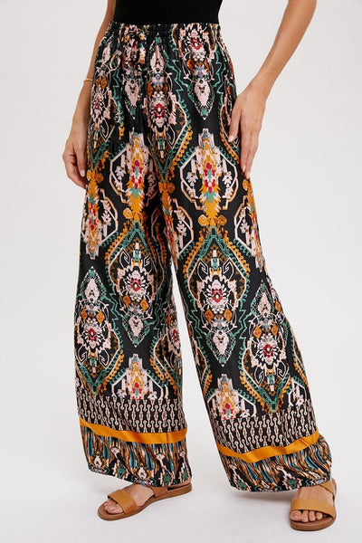 Cool, comfy and versatile! These woven wide leg pants are that and more! Featuring an all over black border print, elastic waist with tassels, and side pockets. Product Details: 100% Polyester Flowy silhouette Side pockets Elastic waist with draw string tie Wide leg