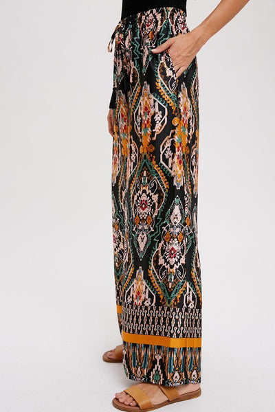 Cool, comfy and versatile! These woven wide leg pants are that and more! Featuring an all over black border print, elastic waist with tassels, and side pockets. Product Details: 100% Polyester Flowy silhouette Side pockets Elastic waist with draw string tie Wide leg