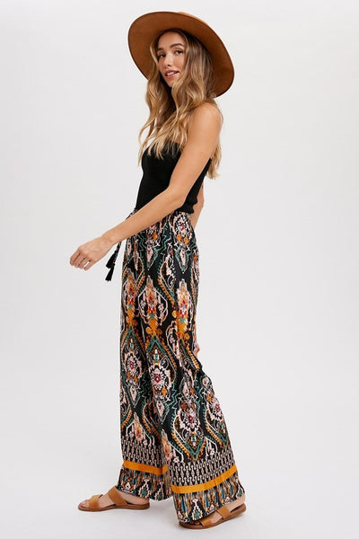 Cool, comfy and versatile! These woven wide leg pants are that and more! Featuring an all over black border print, elastic waist with tassels, and side pockets. Product Details: 100% Polyester Flowy silhouette Side pockets Elastic waist with draw string tie Wide leg
