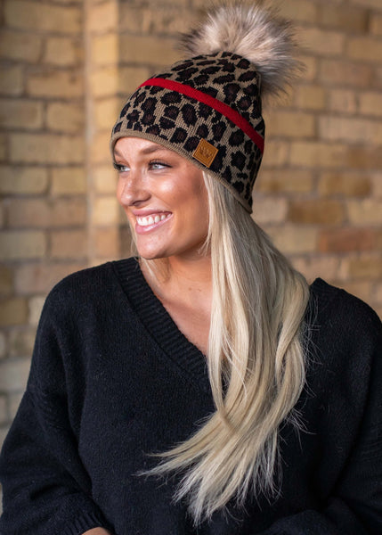 Stand out in this leopard pattern fleece lined knit hat. The red stripe detail and faux fur pom accent takes this winter hat up a notch.
