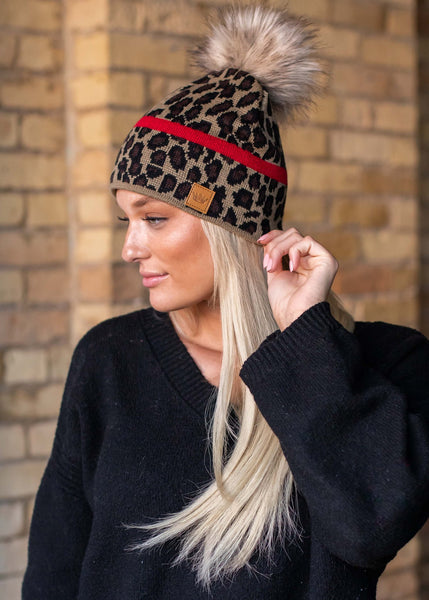 Stand out in this leopard pattern fleece lined knit hat. The red stripe detail and faux fur pom accent takes this winter hat up a notch.