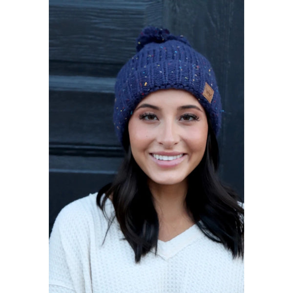 Keep your melon warm in this fleece lined navy speckled hat. Featuring a fun pom pom at the top and attractive large braided knit pattern. Product Details: 90% Acrylic, 10% Polyester, Lining 100% Polyester Fold down cuff Comfy fleece lining