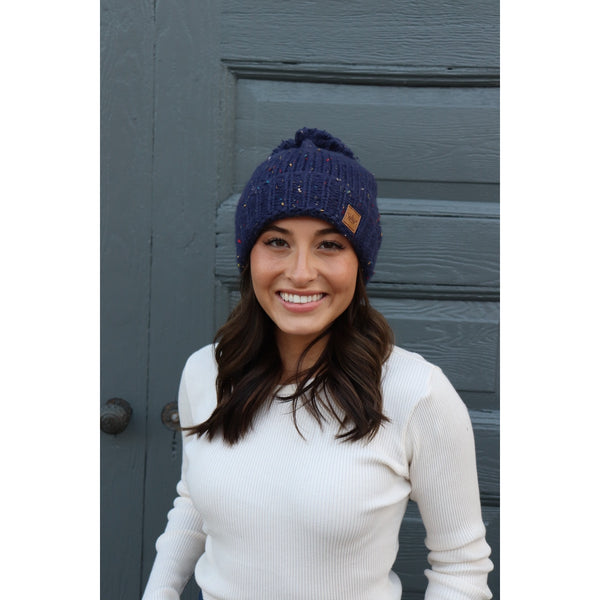 Keep your melon warm in this fleece lined navy speckled hat. Featuring a fun pom pom at the top and attractive large braided knit pattern. Product Details: 90% Acrylic, 10% Polyester, Lining 100% Polyester Fold down cuff Comfy fleece lining