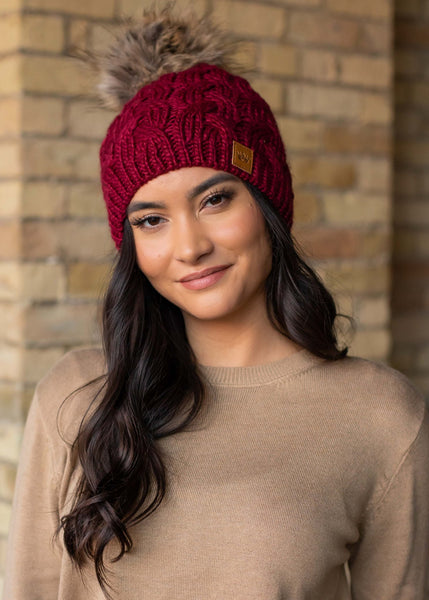 This stunning wine color cable knit fleece lined hat with keep your head warm and stylish! Product Details: 100% Acrylic, Lining 100% Polyester Knit hat Comfy fleece lining Faux fur pom accent
