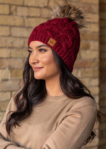 This stunning wine color cable knit fleece lined hat with keep your head warm and stylish! Product Details: 100% Acrylic, Lining 100% Polyester Knit hat Comfy fleece lining Faux fur pom accent
