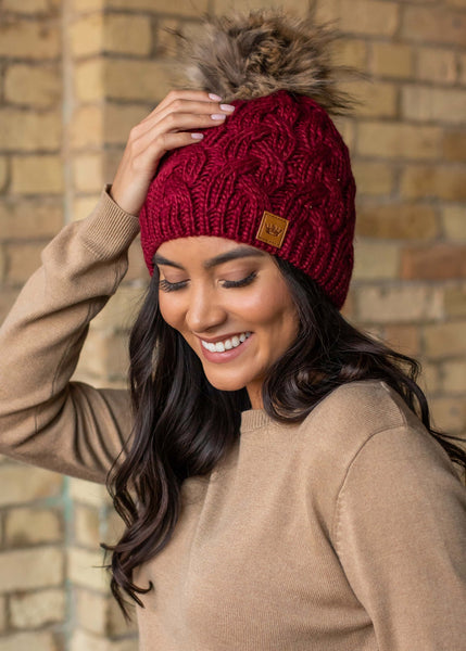 This stunning wine color cable knit fleece lined hat with keep your head warm and stylish! Product Details: 100% Acrylic, Lining 100% Polyester Knit hat Comfy fleece lining Faux fur pom accent