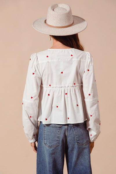 Fall in love with the romantic charm of this ivory blouse, adorned with delicate red heart embroidery that adds a playful pop of color. Featuring an elegant front-tie detail and feminine puff sleeves, this top strikes the perfect balance between sweet and sophisticated. The lightweight fabric drapes beautifully, making it ideal for date nights, casual outings, or festive occasions. Pair it with your favorite jeans, skirts, or tailored trousers to create a look that’s effortlessly chic and full of love!