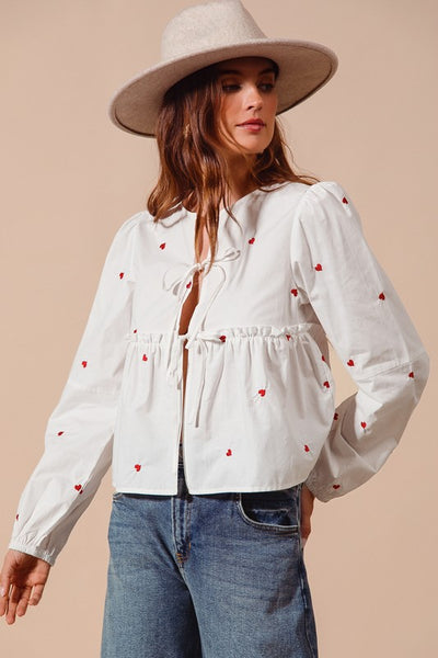 Fall in love with the romantic charm of this ivory blouse, adorned with delicate red heart embroidery that adds a playful pop of color. Featuring an elegant front-tie detail and feminine puff sleeves, this top strikes the perfect balance between sweet and sophisticated. The lightweight fabric drapes beautifully, making it ideal for date nights, casual outings, or festive occasions. Pair it with your favorite jeans, skirts, or tailored trousers to create a look that’s effortlessly chic and full of love!