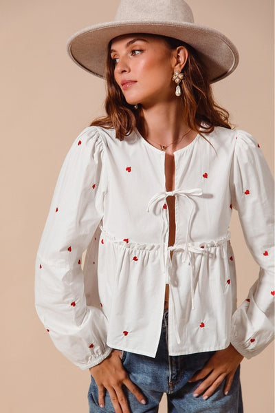 Fall in love with the romantic charm of this ivory blouse, adorned with delicate red heart embroidery that adds a playful pop of color. Featuring an elegant front-tie detail and feminine puff sleeves, this top strikes the perfect balance between sweet and sophisticated. The lightweight fabric drapes beautifully, making it ideal for date nights, casual outings, or festive occasions. Pair it with your favorite jeans, skirts, or tailored trousers to create a look that’s effortlessly chic and full of love!