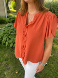 This Romantic Rust Top is ideal for adding an air of luxe elegance to any outfit. Its wraparound short sleeves, V-neck with collar stand, and ruffle details on the center front create an idyllic silhouette for any occasion, while the textured fabric ensures a comfortable fit. Show off your sophistication in this chic top.  Product Details:  Short sleeve ruffle top Button up front Rust color