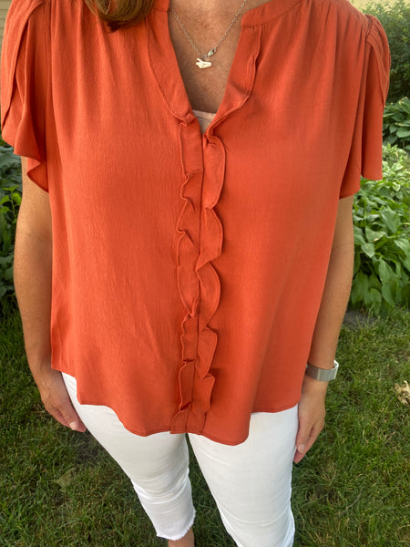 This Romantic Rust Top is ideal for adding an air of luxe elegance to any outfit. Its wraparound short sleeves, V-neck with collar stand, and ruffle details on the center front create an idyllic silhouette for any occasion, while the textured fabric ensures a comfortable fit. Show off your sophistication in this chic top.  Product Details:  Short sleeve ruffle top Button up front Rust color