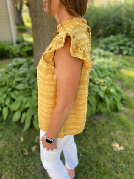 You need to add our Maddy Ruffle Top to your wardrobe! This playful piece features a high neck band, flouncy ruffle sleeves, and a tie and keyhole detail in the back. This stunning mustard color pairs well with white or classic denim.   Product Details:  Stripe burn out woven fabric Flouncy ruffle short sleeves Tie and keyhole back High neck