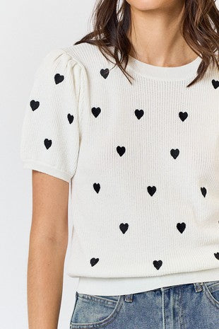 Fall in love with our Heart Short Sleeve Sweater! This playful sweater features a heart embroidery design and puffed sleeves for a unique touch. Made with a soft cotton and acrylic blend, it's comfortable and stylish. Perfect for adding a dose of love to any outfit.  Product Details:  60% Cotton, 40% Acrylic Black embroidered heart