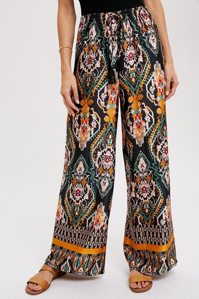 Cool, comfy and versatile! These woven wide leg pants are that and more! Featuring an all over black border print, elastic waist with tassels, and side pockets.  Product Details:  100% Polyester Flowy silhouette Side pockets Elastic waist with draw string tie Wide leg