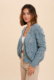 This feminine hand knit sage green cardigan is so sweet. Featuring a cable knit with pom poms and scalloped bottom.  Pairs perfectly with a white tee and denim for a instantly chic look.   Product Details:  50% Acrylic, 28% Recycled Polyester, 22% Polyester Cardigan with button front closure Shorter length