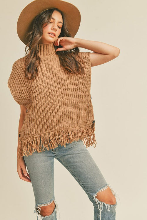 This sleeveless taupe fringe poncho vest has a slight boho vibe. Featuring a mock neck and open at the sides with button closure. Pair with a long sleeve top as the temperatures dip and your favorite pair of jeans.   Product Details:  Fabric is 100% Acrylic Ribbed high neckline Fringe hem Side button closure Boxy silhouette Model is 5' 9" 33-25.5-36 and wears a S