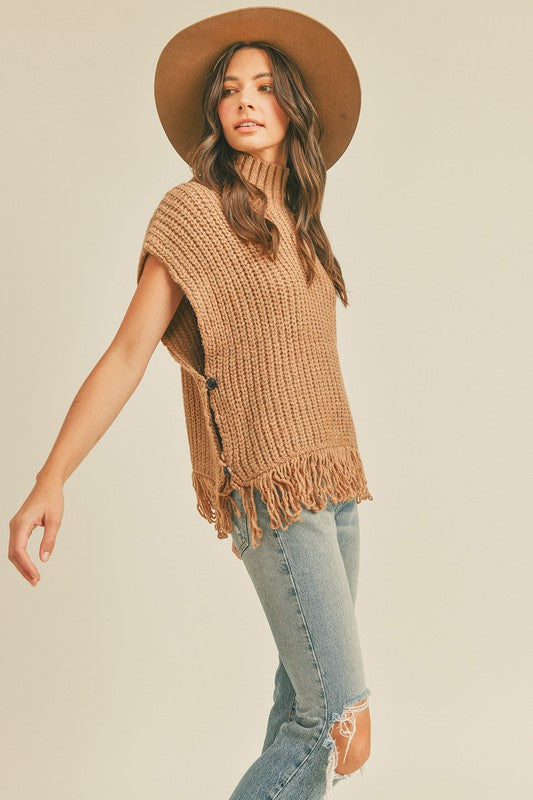 This sleeveless taupe fringe poncho vest has a slight boho vibe. Featuring a mock neck and open at the sides with button closure. Pair with a long sleeve top as the temperatures dip and your favorite pair of jeans.   Product Details:  Fabric is 100% Acrylic Ribbed high neckline Fringe hem Side button closure Boxy silhouette Model is 5' 9" 33-25.5-36 and wears a S